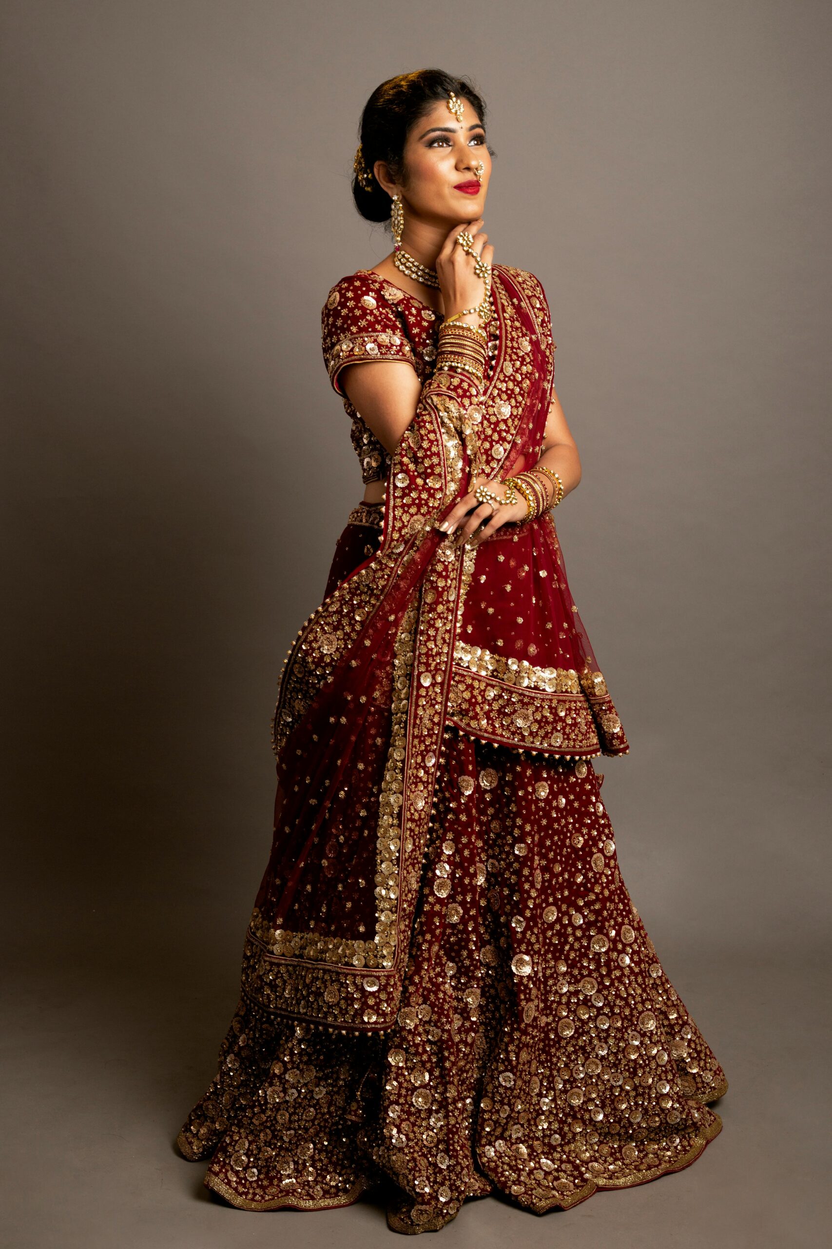Portrait of an Indian woman in bridal dress against a grey background, showcasing elegance.
